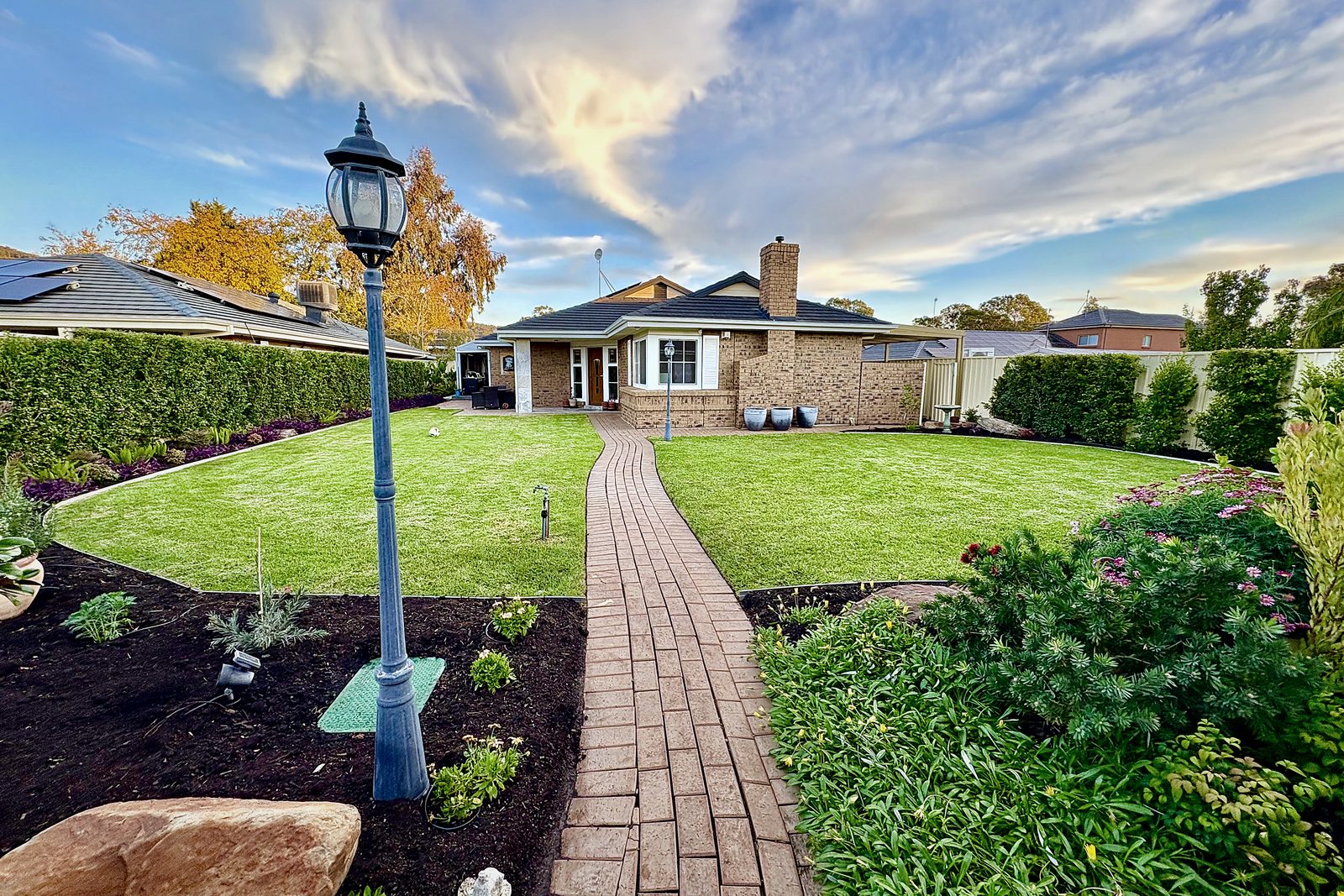 The same garden after Iris — lush striped lawn, mulched beds and manicured hedges