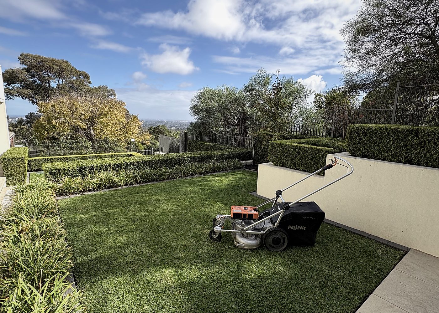 Pellenc battery-powered mower on a freshly cut, hedged lawn under a blue sky